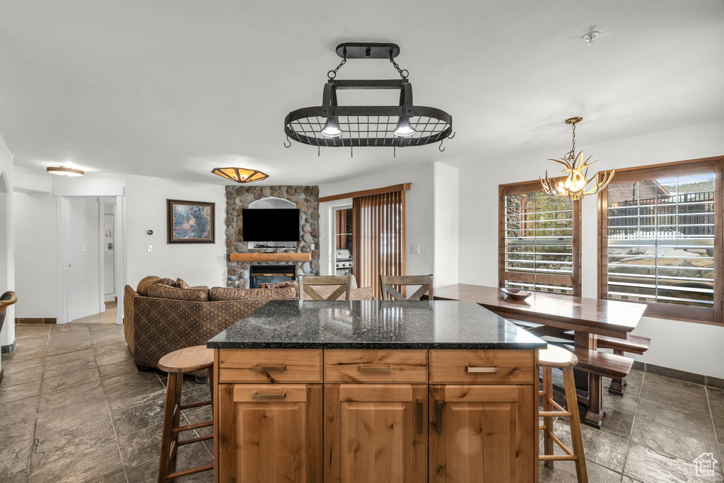 Kitchen featuring pendant lighting, dark stone counters, a chandelier, dark tile floors, and a stone fireplace