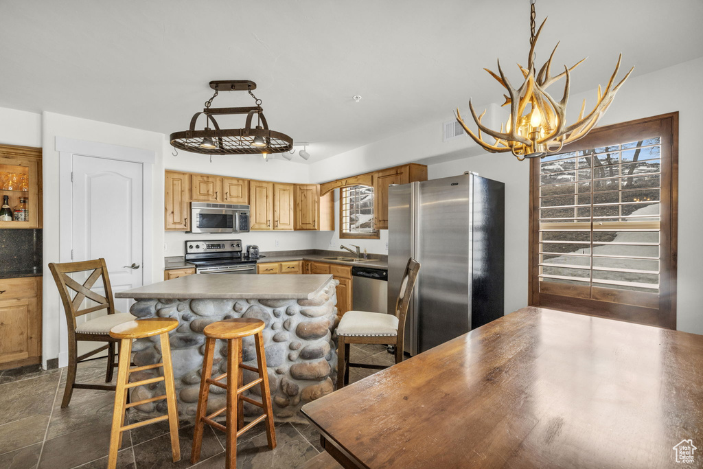 Kitchen featuring hanging light fixtures, sink, stainless steel appliances, a center island, and a chandelier