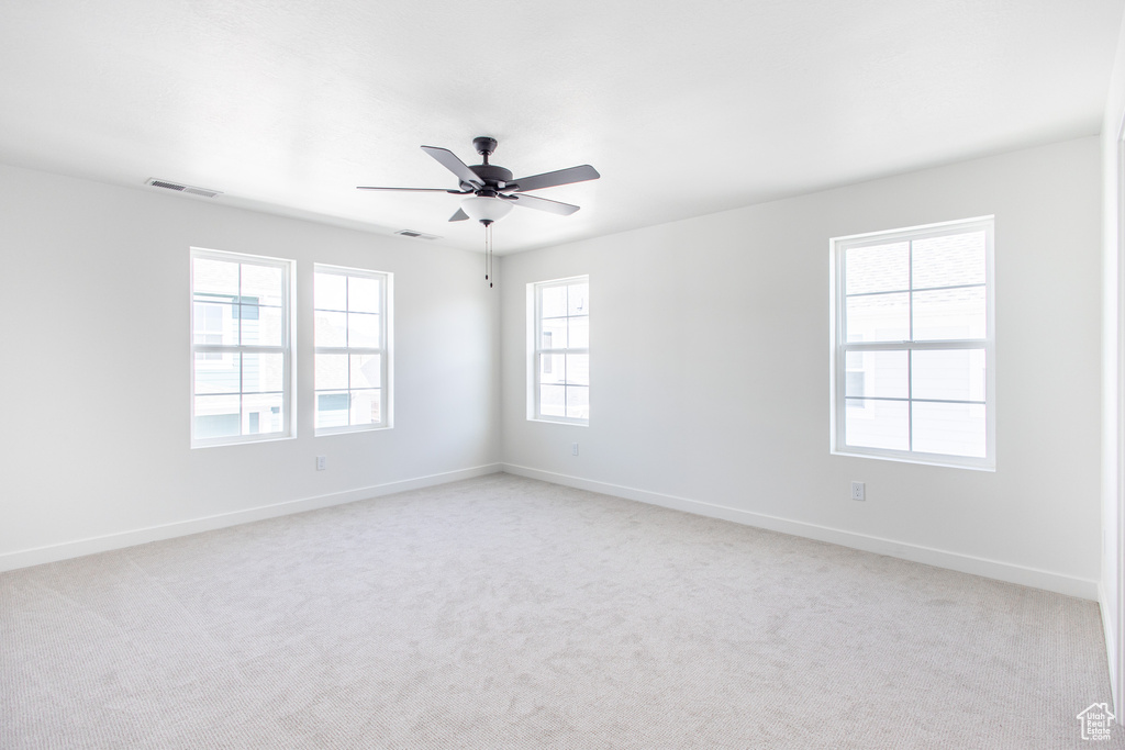 Carpeted spare room featuring a healthy amount of sunlight and ceiling fan