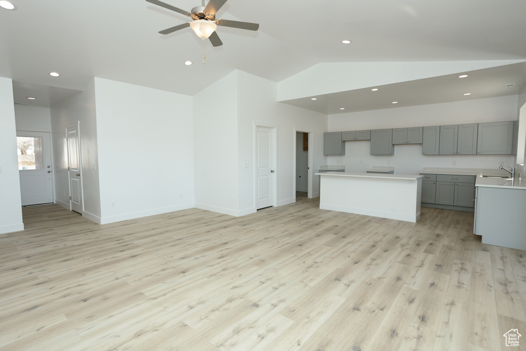 Unfurnished living room featuring sink, light hardwood / wood-style floors, ceiling fan, and lofted ceiling