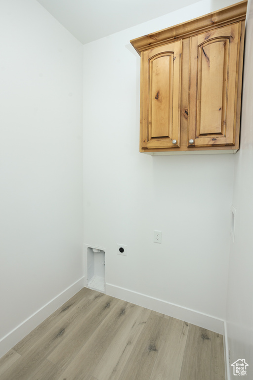Washroom with light wood-type flooring, hookup for an electric dryer, and cabinets
