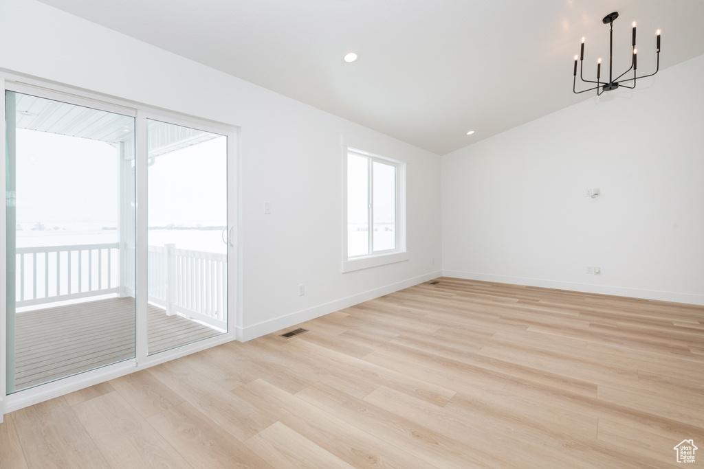 Empty room featuring a chandelier, light hardwood / wood-style floors, and lofted ceiling