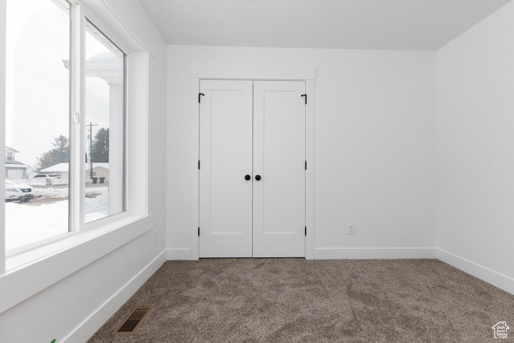 Unfurnished bedroom with multiple windows, a closet, and dark carpet