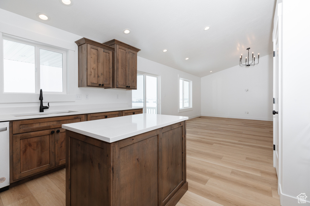 Kitchen with light wood-type flooring, a notable chandelier, a kitchen island, dishwashing machine, and sink