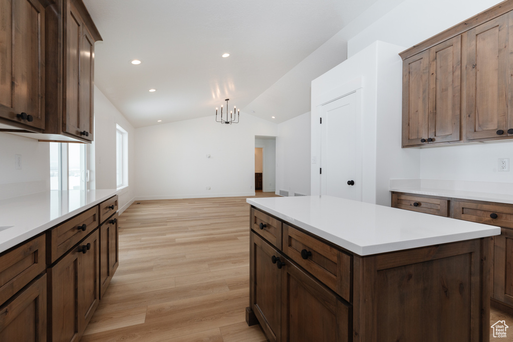 Kitchen featuring light wood-type flooring, a notable chandelier, a kitchen island, vaulted ceiling, and decorative light fixtures