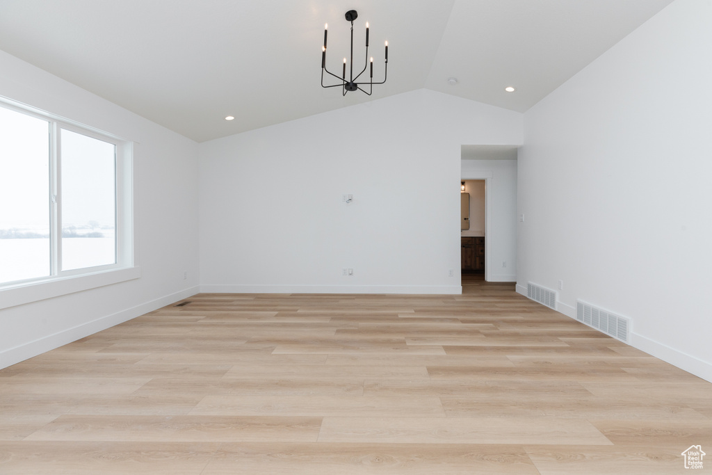 Empty room featuring an inviting chandelier, light hardwood / wood-style floors, and vaulted ceiling