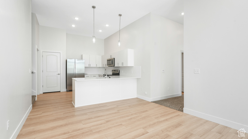 Kitchen featuring light hardwood / wood-style flooring, white cabinets, a high ceiling, appliances with stainless steel finishes, and pendant lighting