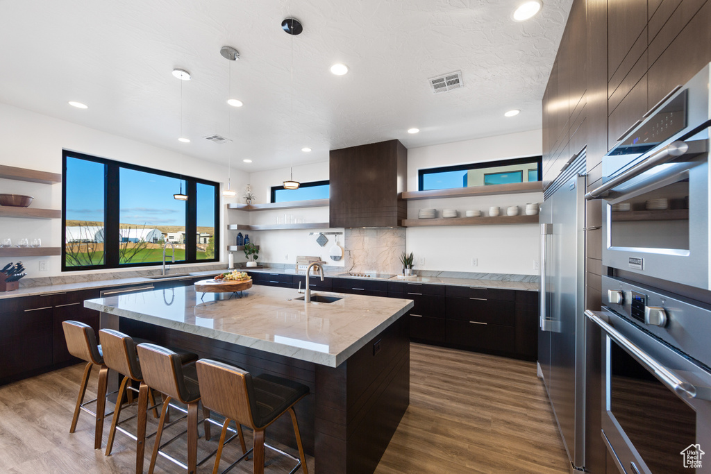 Kitchen featuring a kitchen island with sink, a breakfast bar, light stone countertops, light hardwood / wood-style flooring, and tasteful backsplash