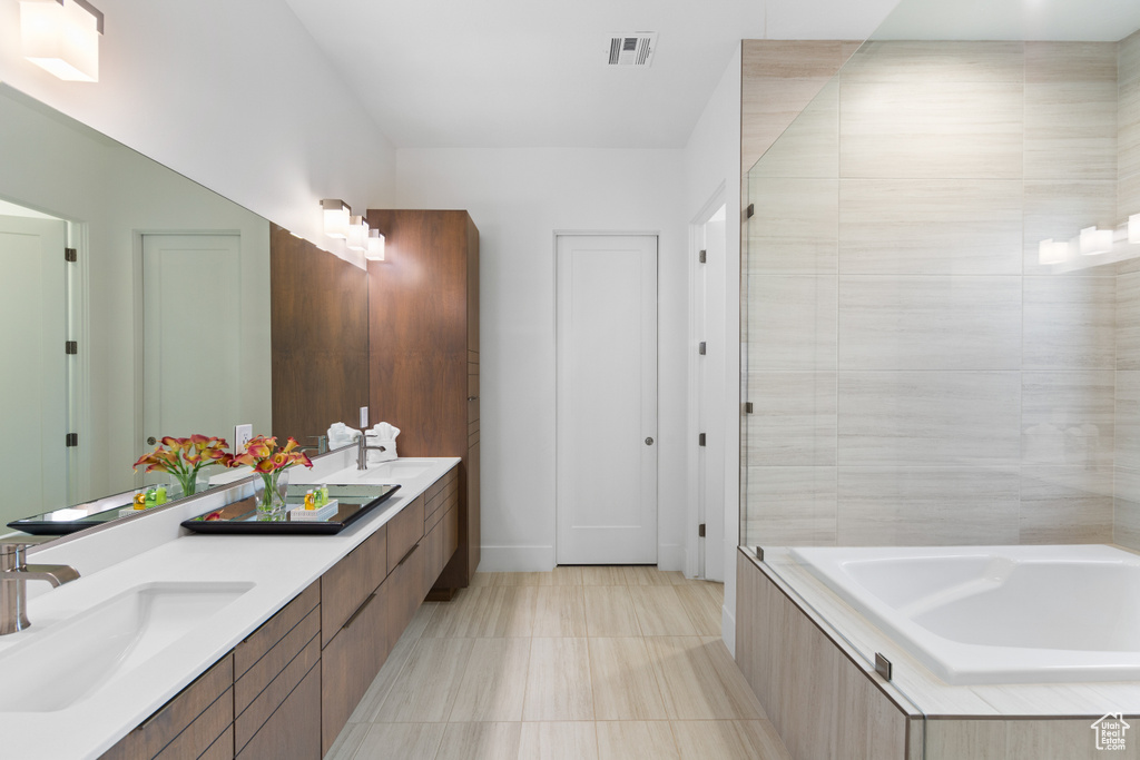 Bathroom featuring a bathtub, dual bowl vanity, and tile flooring