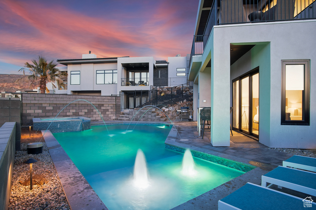 Pool at dusk with pool water feature and a patio area