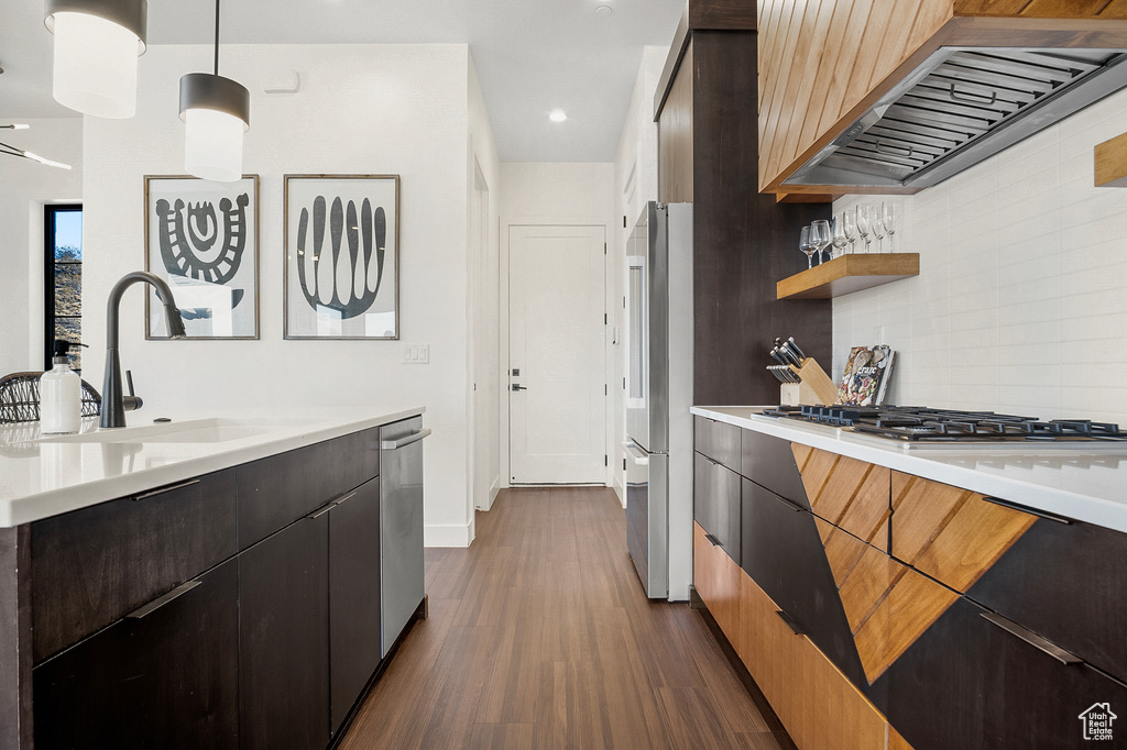Kitchen with sink, dark wood-type flooring, hanging light fixtures, stainless steel appliances, and premium range hood