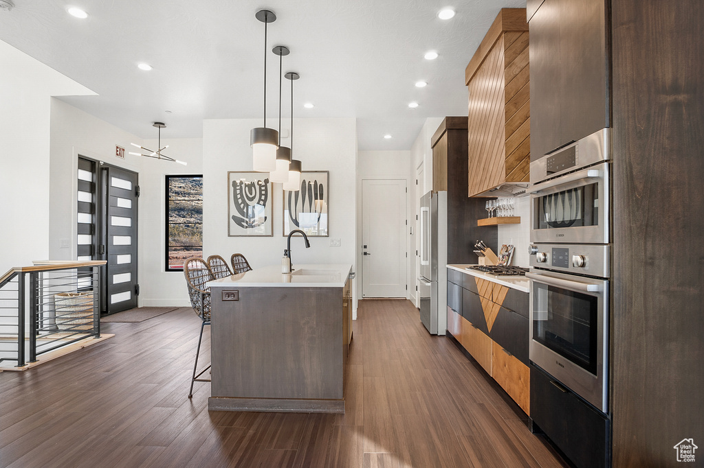 Kitchen featuring a kitchen breakfast bar, stainless steel appliances, dark hardwood / wood-style floors, and hanging light fixtures