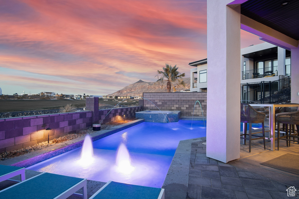 Pool at dusk with a mountain view, pool water feature, and a patio