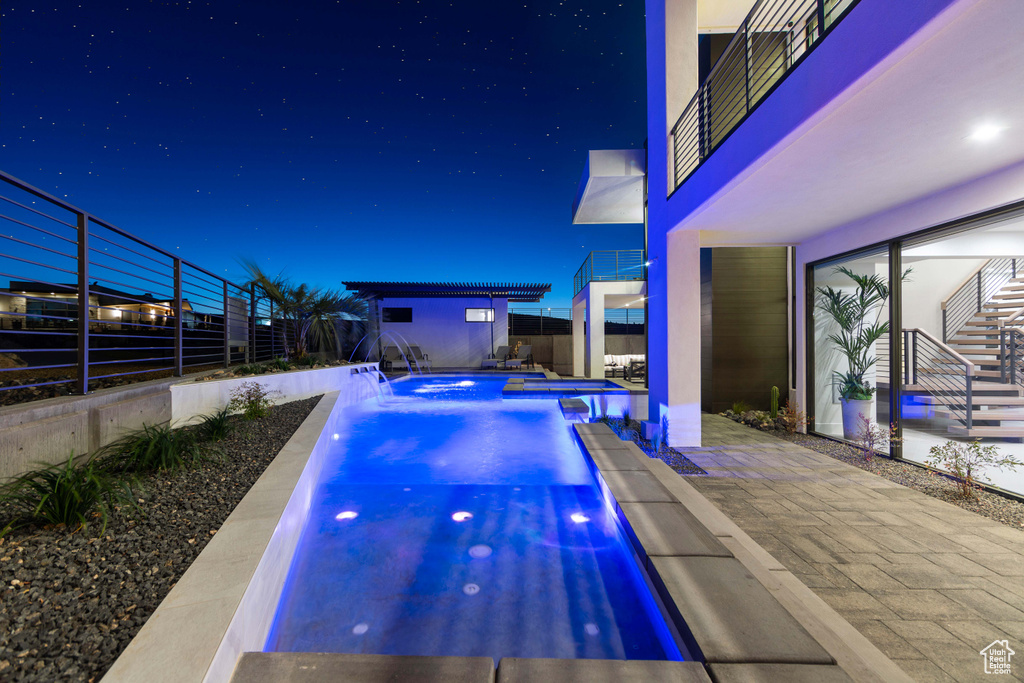 Pool at night with a patio, a hot tub, and pool water feature