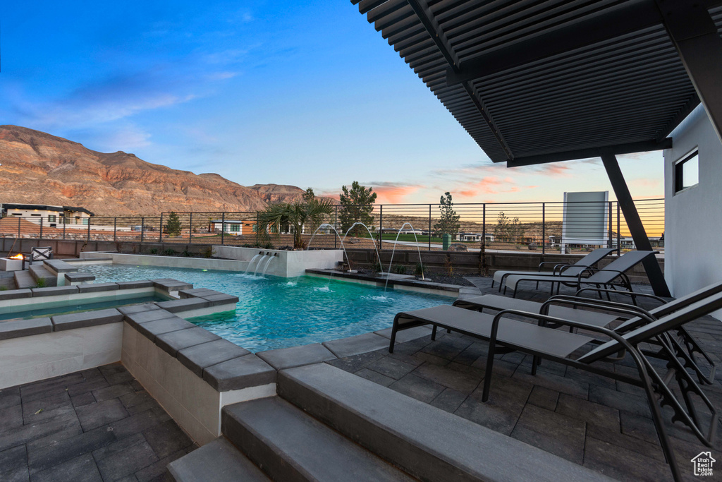 Pool at dusk with a patio area, pool water feature, a mountain view, and an in ground hot tub
