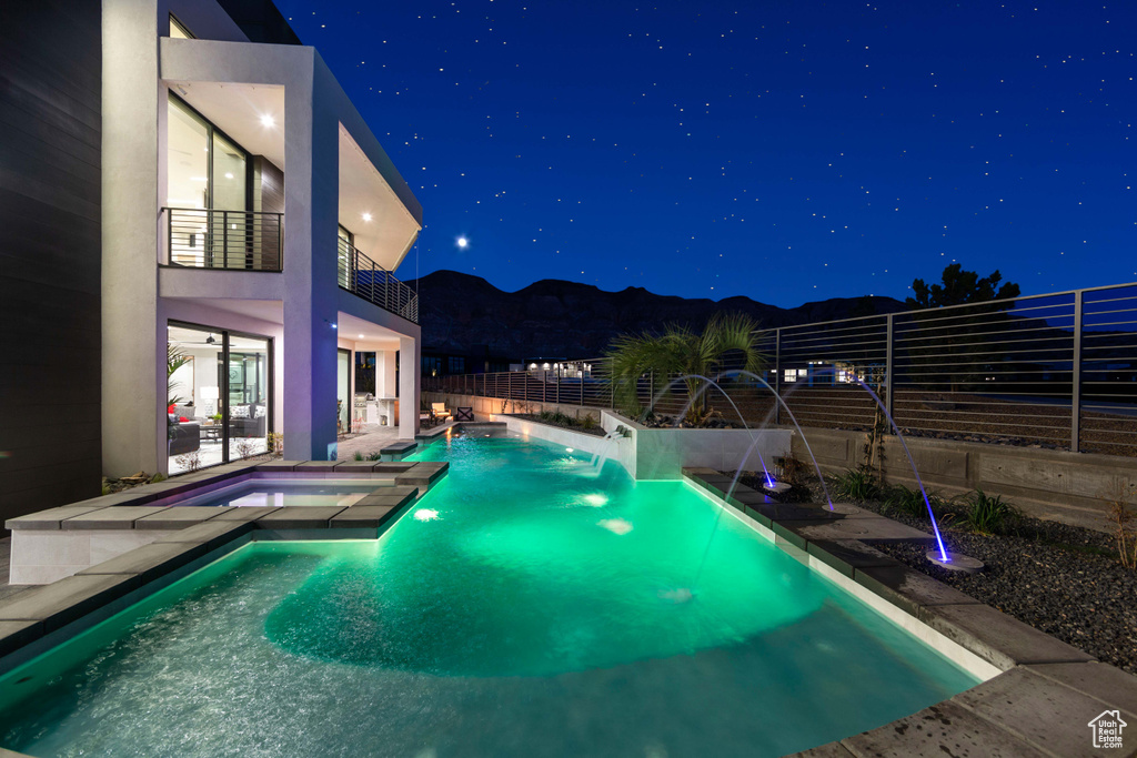 Pool at night featuring a patio, pool water feature, and an in ground hot tub