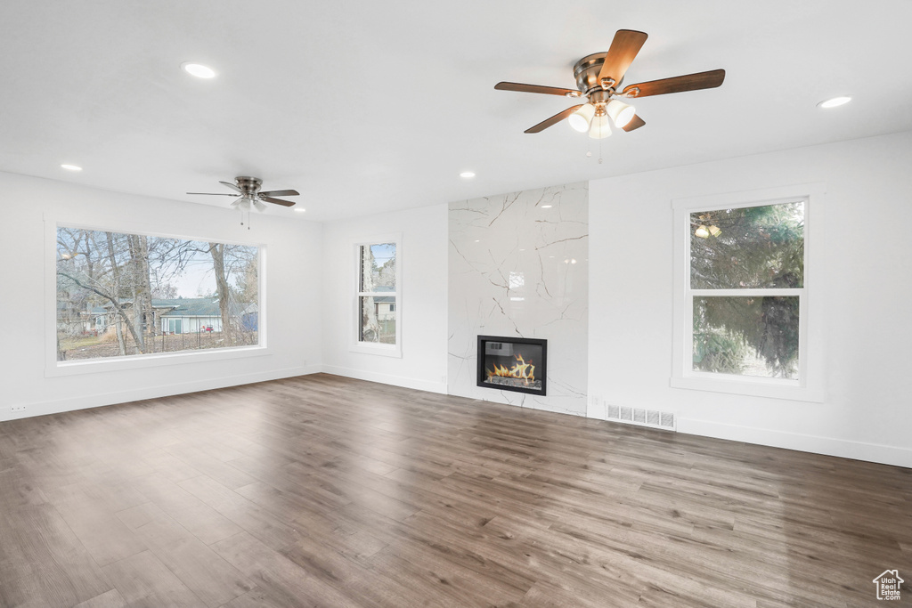 Unfurnished living room featuring dark wood-type flooring, plenty of natural light, a fireplace, and ceiling fan