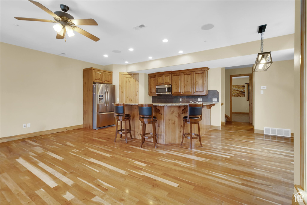 Kitchen featuring light hardwood / wood-style floors, ceiling fan, stainless steel appliances, and backsplash