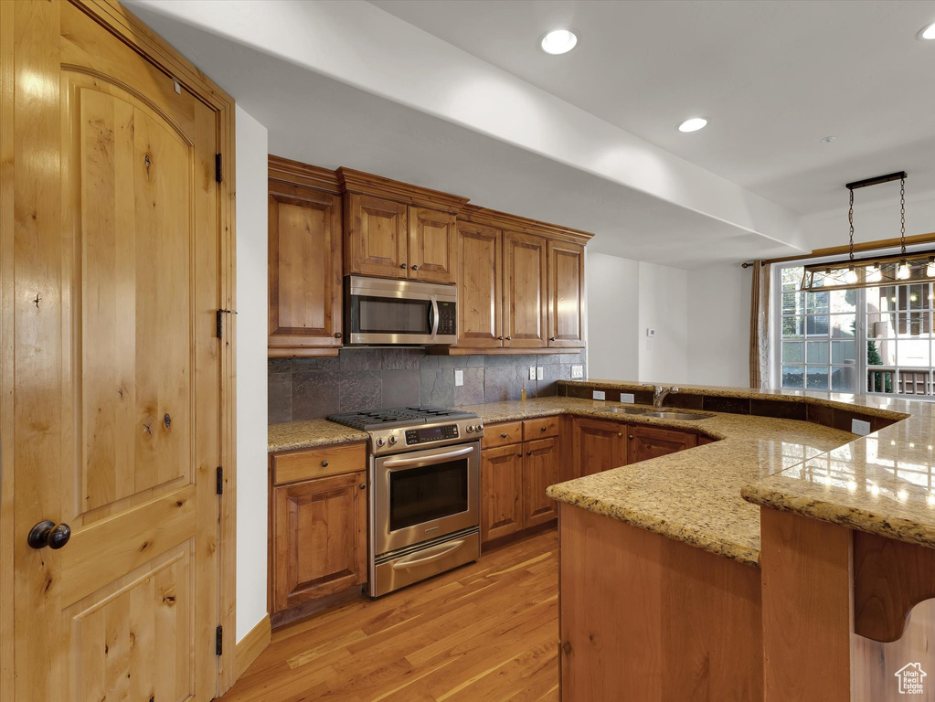 Kitchen with pendant lighting, light hardwood / wood-style flooring, backsplash, appliances with stainless steel finishes, and light stone counters