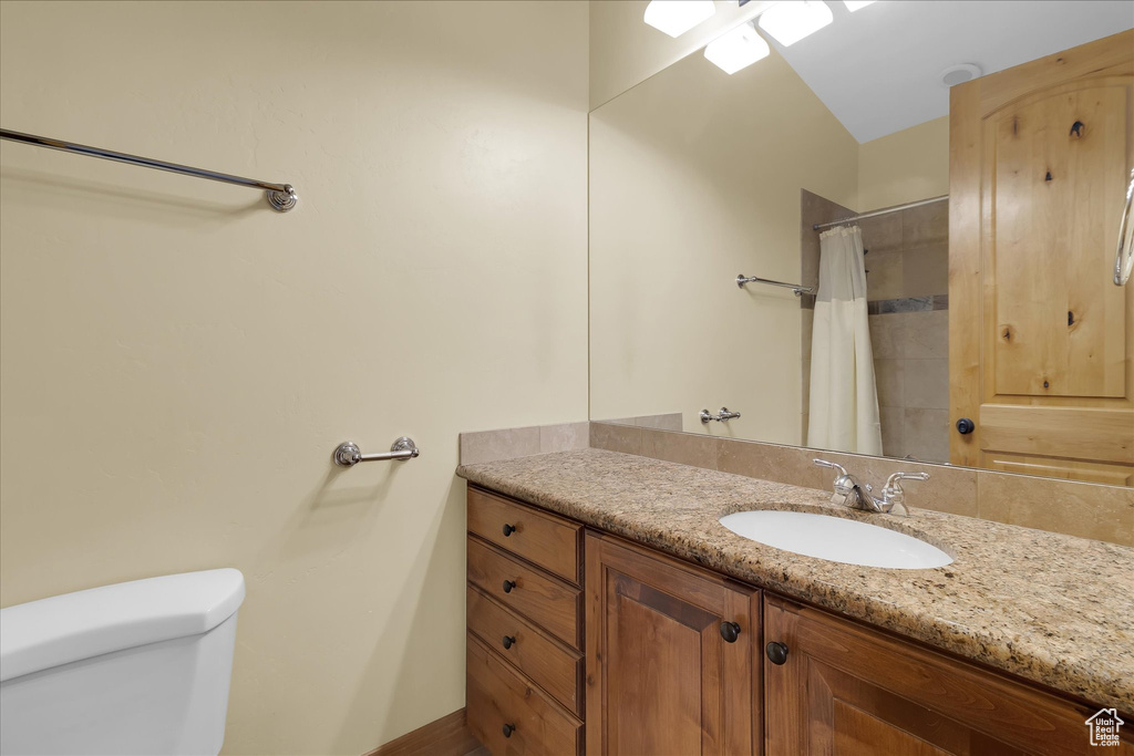 Bathroom with large vanity, vaulted ceiling, and toilet