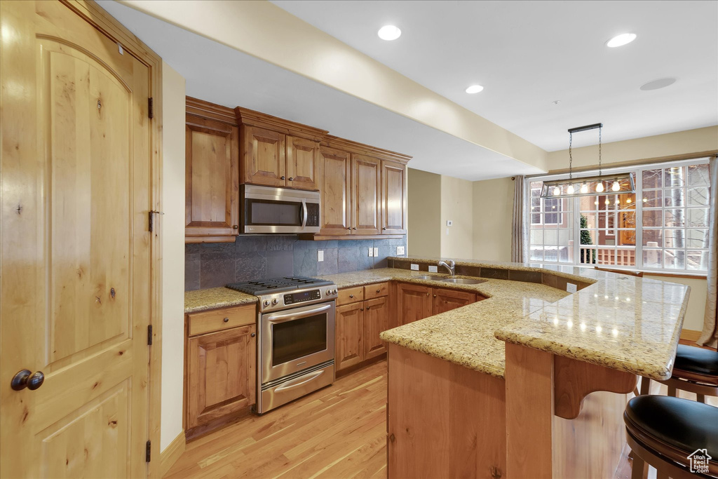 Kitchen featuring stainless steel appliances, backsplash, hanging light fixtures, light hardwood / wood-style floors, and sink