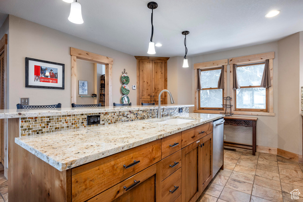 Kitchen featuring sink, light tile floors, light stone counters, hanging light fixtures, and backsplash