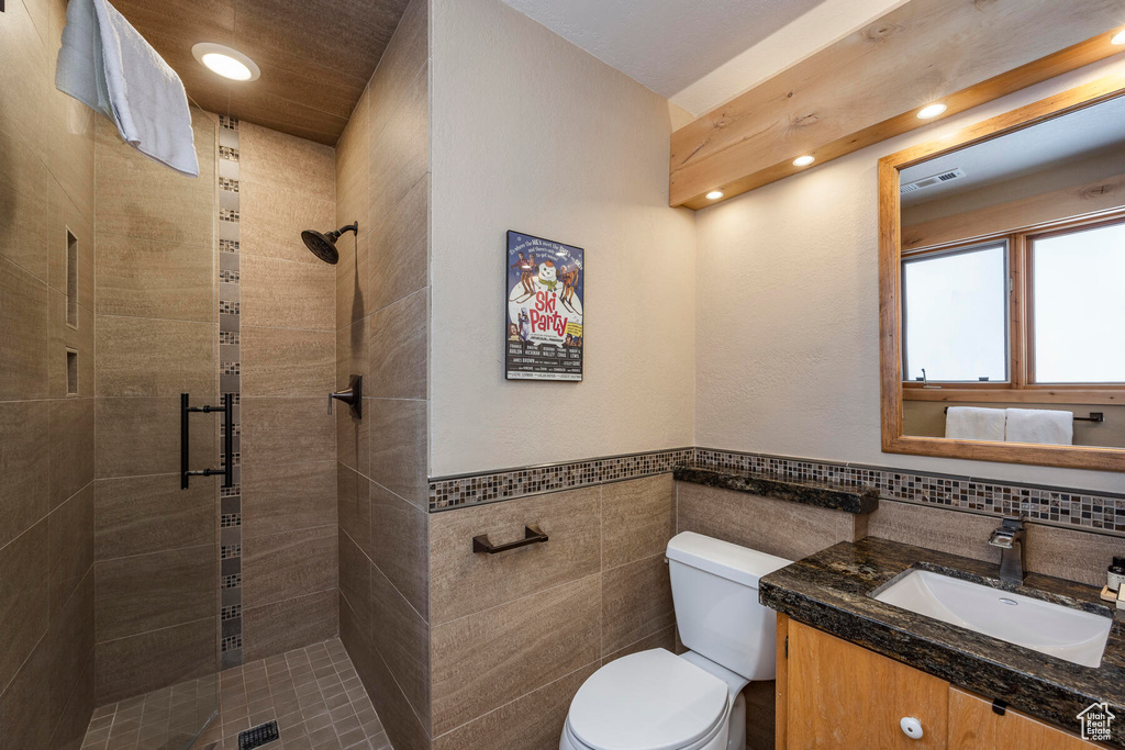 Bathroom featuring toilet, an enclosed shower, vanity, and tile walls