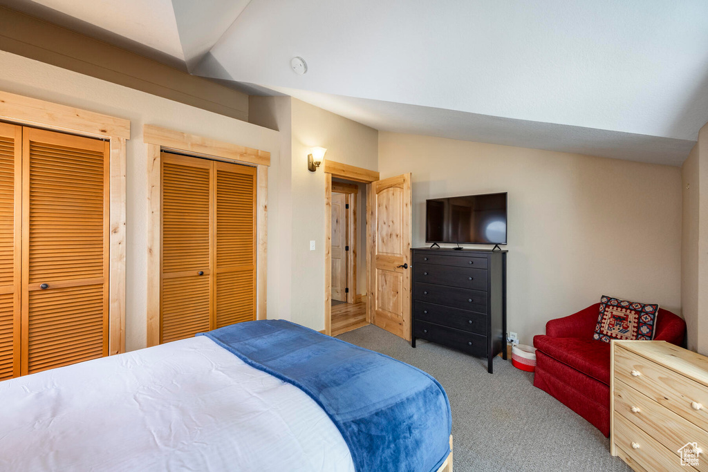 Bedroom featuring multiple closets, light carpet, and vaulted ceiling