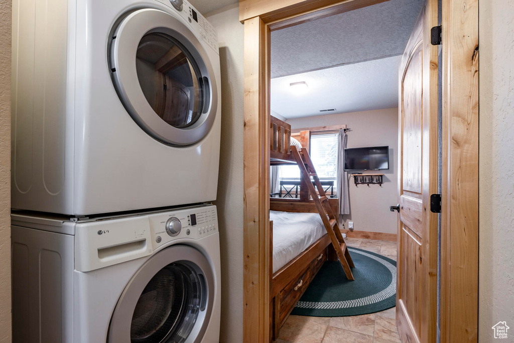 Laundry room with a textured ceiling, stacked washer and clothes dryer, and light tile flooring