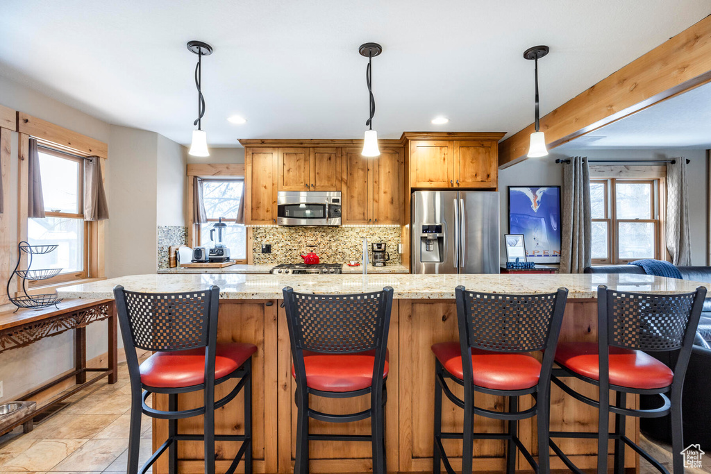 Kitchen featuring hanging light fixtures, stainless steel appliances, a breakfast bar, and a wealth of natural light