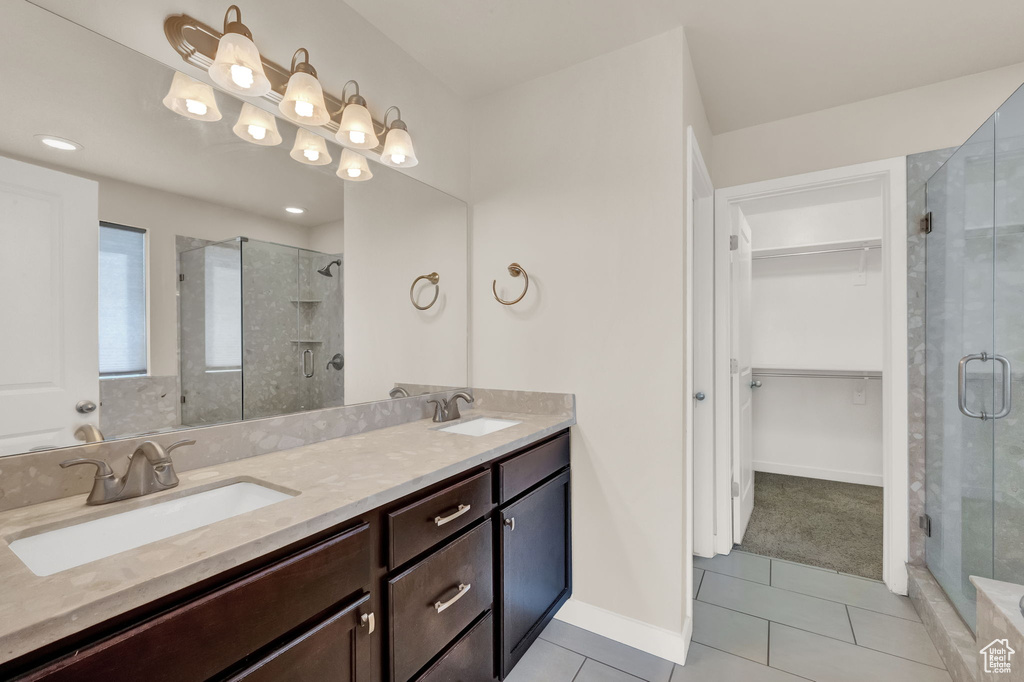 Bathroom featuring dual sinks, a shower with door, vanity with extensive cabinet space, and tile floors