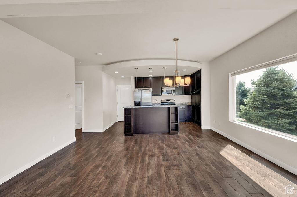 Kitchen with a center island with sink, appliances with stainless steel finishes, dark wood-type flooring, and decorative light fixtures