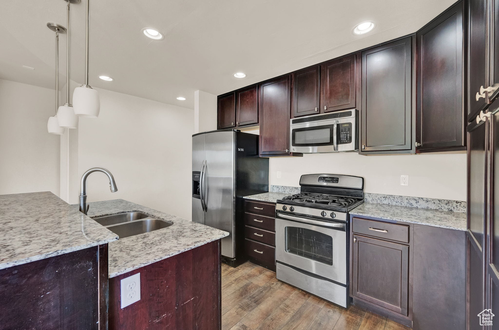 Kitchen featuring hardwood / wood-style floors, stainless steel appliances, light stone countertops, sink, and decorative light fixtures