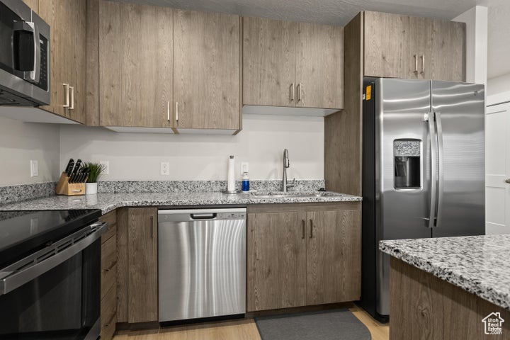 Kitchen with sink, appliances with stainless steel finishes, light stone countertops, and light wood-type flooring