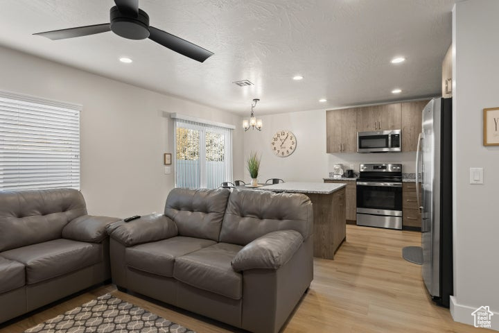 Living room with light hardwood / wood-style flooring and ceiling fan with notable chandelier