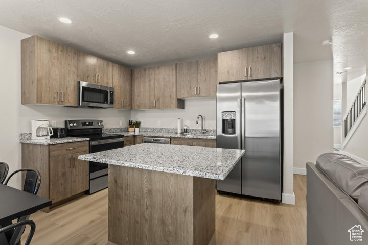 Kitchen with a kitchen island, light wood-type flooring, light stone countertops, sink, and appliances with stainless steel finishes