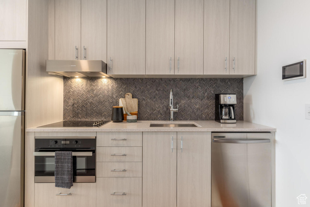 Kitchen with stainless steel appliances, light stone countertops, tasteful backsplash, wall chimney range hood, and sink