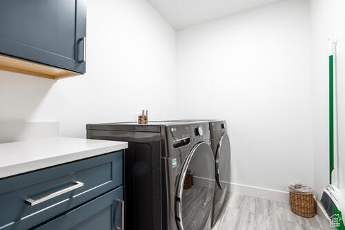 Clothes washing area featuring light hardwood / wood-style floors, washing machine and dryer, and cabinets