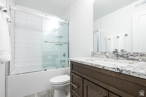 Full bathroom with bath / shower combo with glass door, toilet, hardwood / wood-style flooring, and vanity with extensive cabinet space