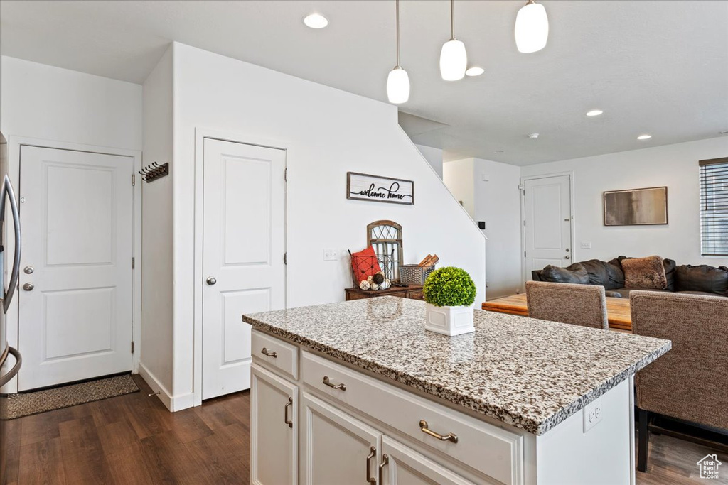 Kitchen featuring dark hardwood / wood-style flooring, light stone counters, white cabinets, a kitchen island, and decorative light fixtures