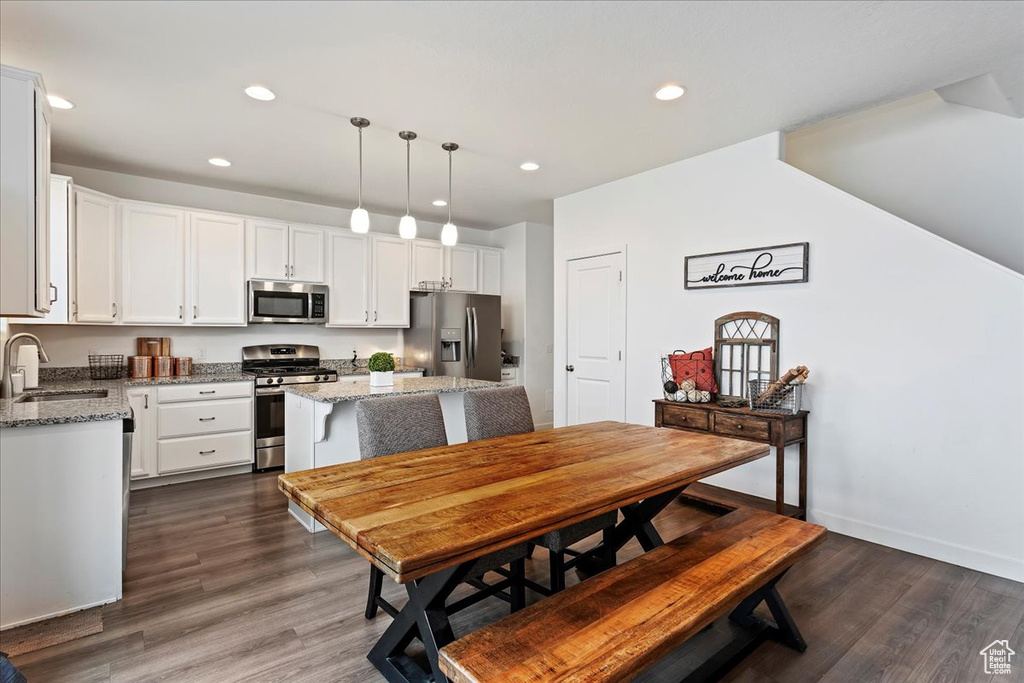 Kitchen featuring hanging light fixtures, dark wood-type flooring, stainless steel appliances, and white cabinetry