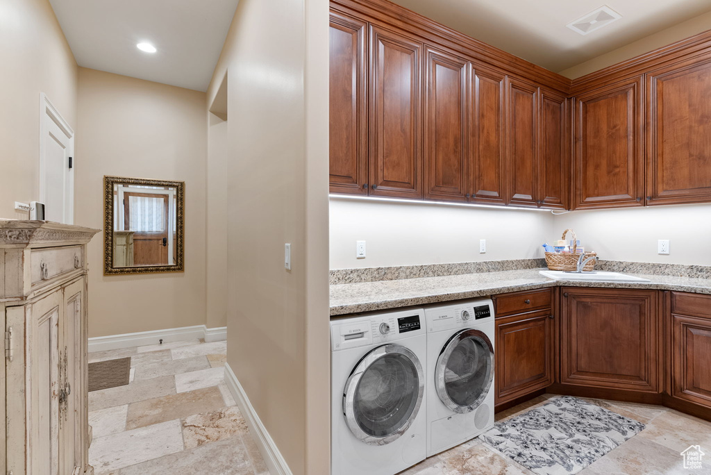 Clothes washing area with cabinets, light tile flooring, sink, and washing machine and dryer
