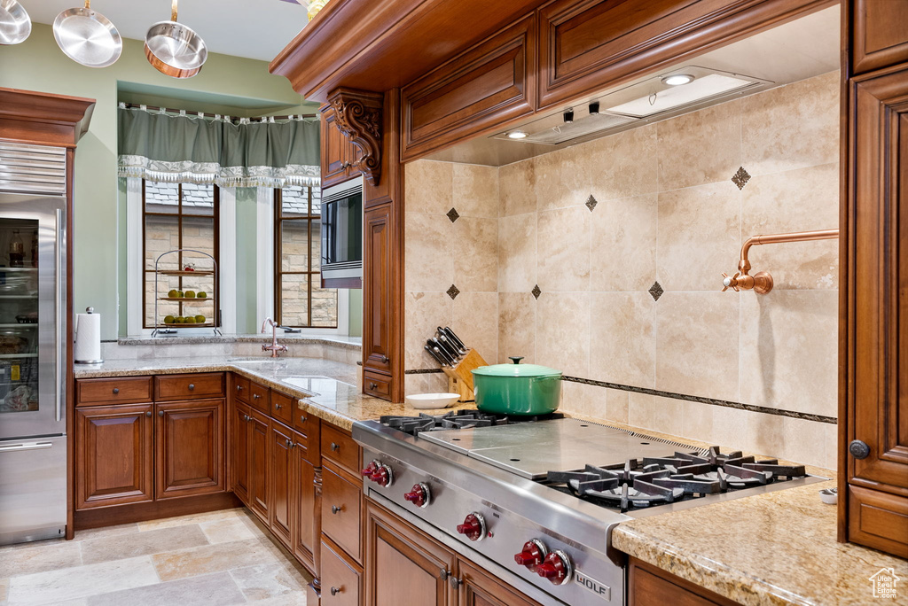 Kitchen with pendant lighting, built in appliances, light stone countertops, tile walls, and light tile floors