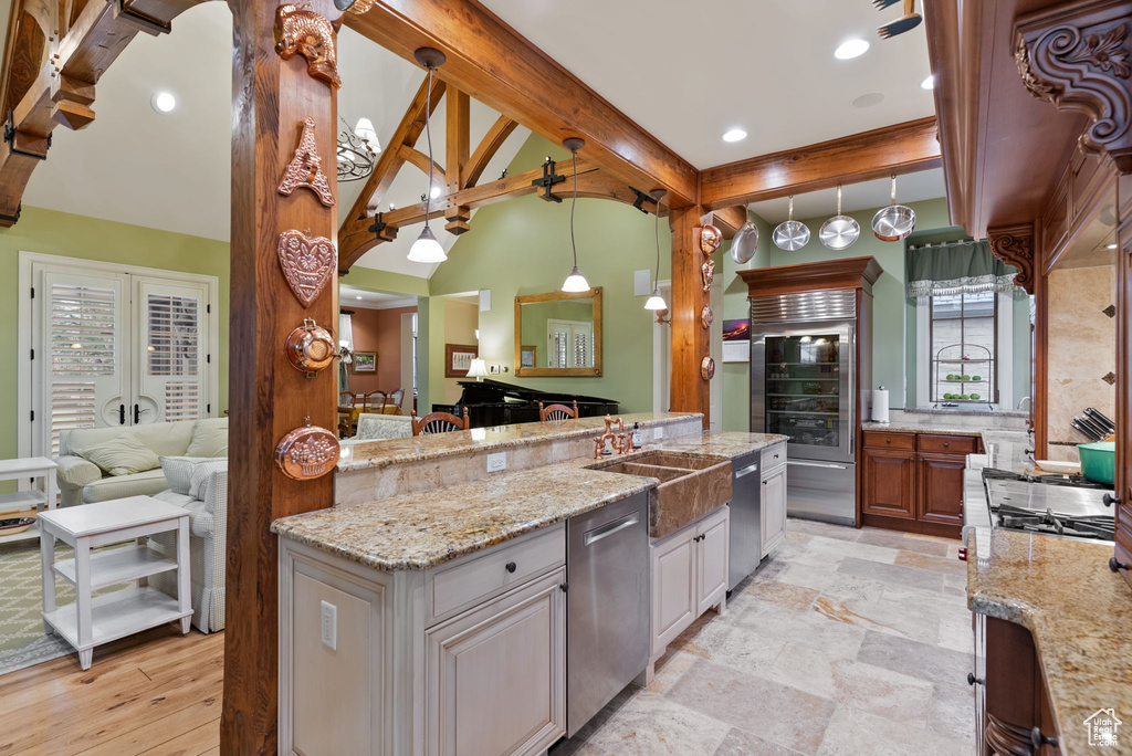 Kitchen featuring light stone countertops, sink, stainless steel appliances, decorative light fixtures, and beam ceiling