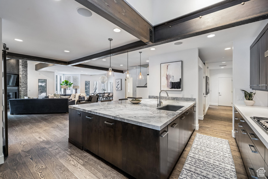 Kitchen with light stone counters, dark hardwood / wood-style flooring, sink, pendant lighting, and beam ceiling