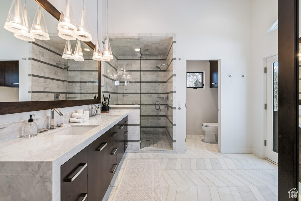 Bathroom with a towering ceiling, oversized vanity, an inviting chandelier, walk in shower, and toilet