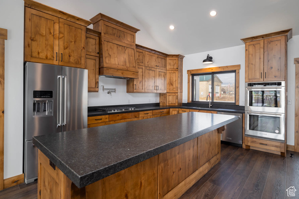 Kitchen with dark hardwood / wood-style flooring, custom range hood, appliances with stainless steel finishes, sink, and a center island
