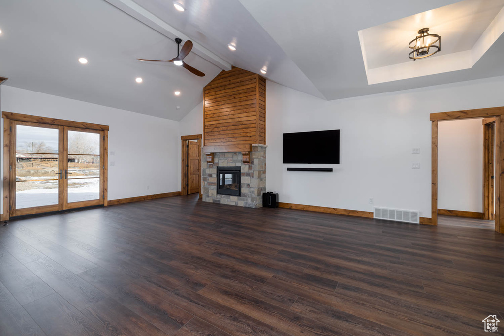 Unfurnished living room featuring dark hardwood / wood-style flooring, french doors, beamed ceiling, a large fireplace, and ceiling fan