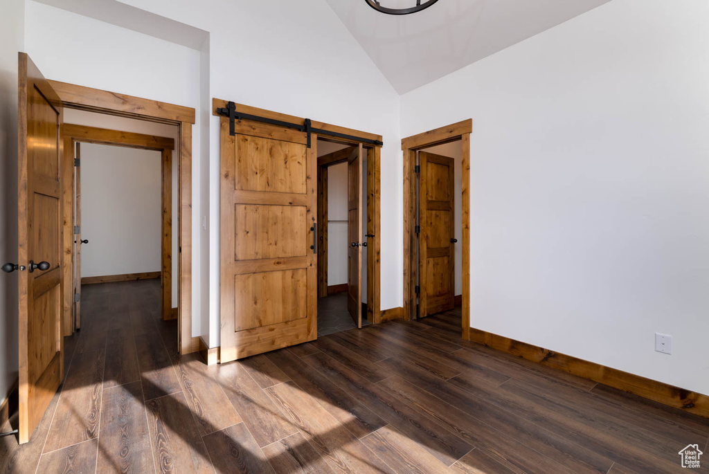 Unfurnished bedroom featuring dark hardwood / wood-style floors, lofted ceiling, and a barn door