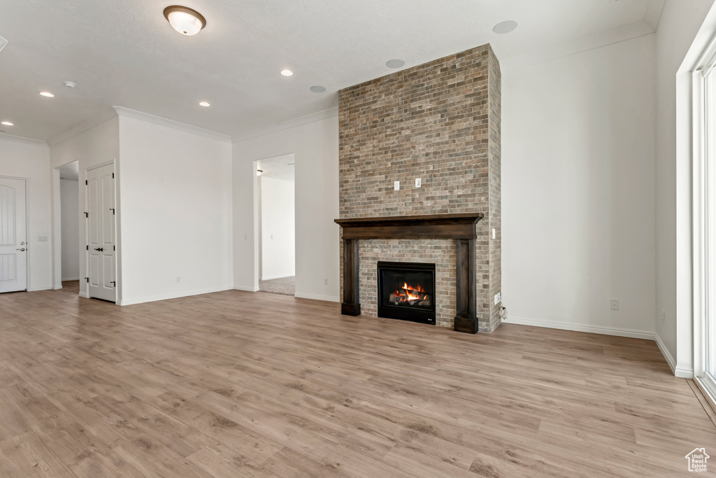 Unfurnished living room with light hardwood / wood-style flooring, crown molding, and a fireplace